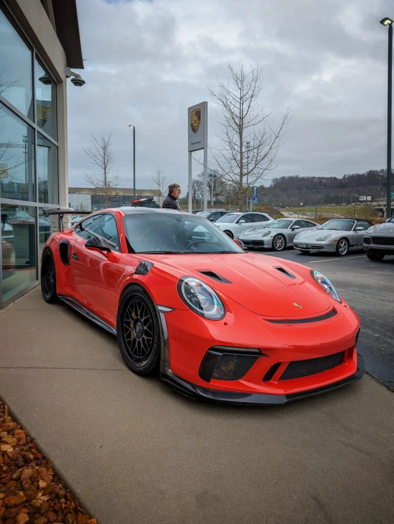 Red Porsche 911 GT3 RS parked outside a dealership with other vehicles visible.