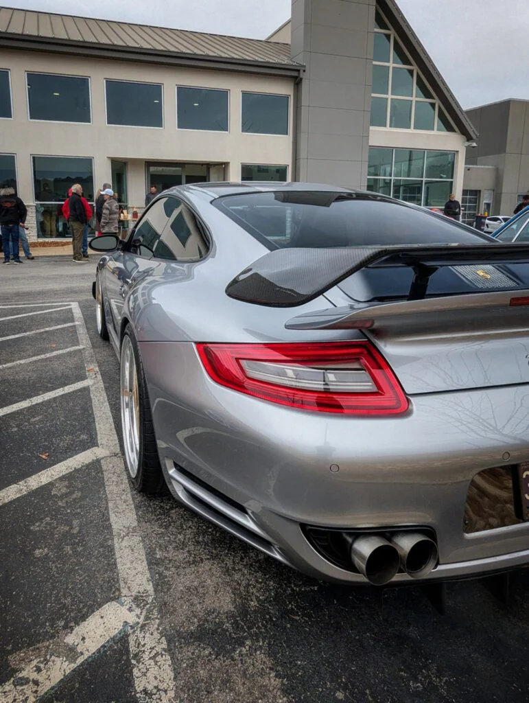 Silver Porsche 911 Turbo parked in front of a modern building with people nearby.