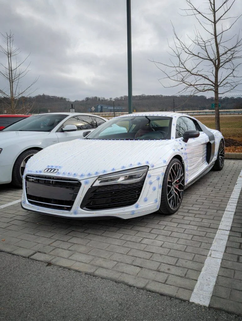 Audi R8 in white camouflage pattern parked among other vehicles in a lot.