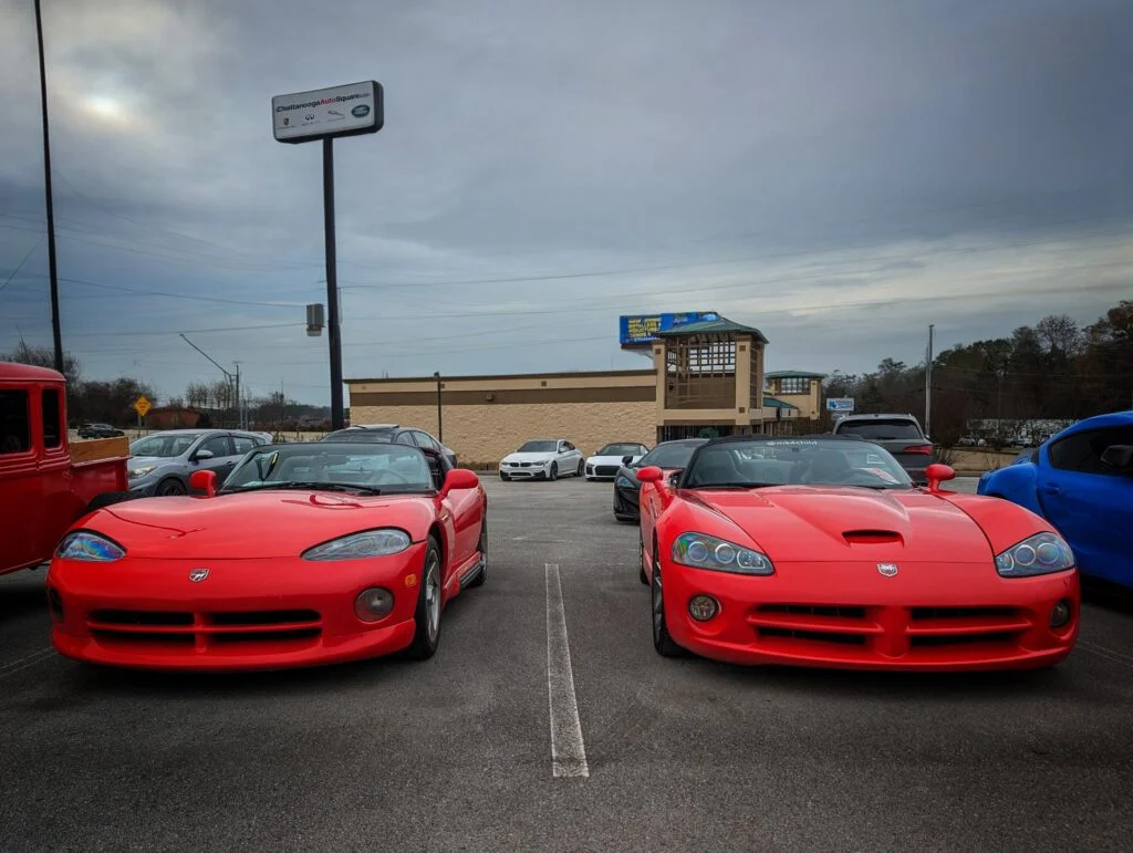 Two red Dodge Vipers parked side by side in a lot with a cloudy sky.