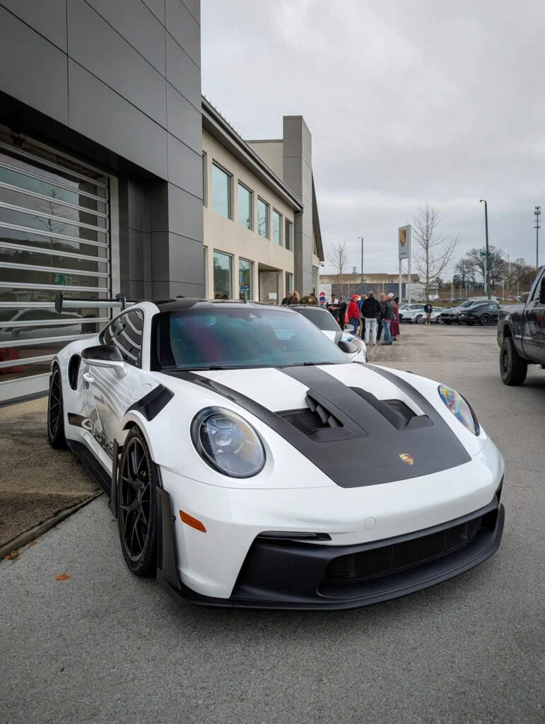 A white Porsche 911 GT3 RS with black carbon fiber accents parked outside a building with people in the background.