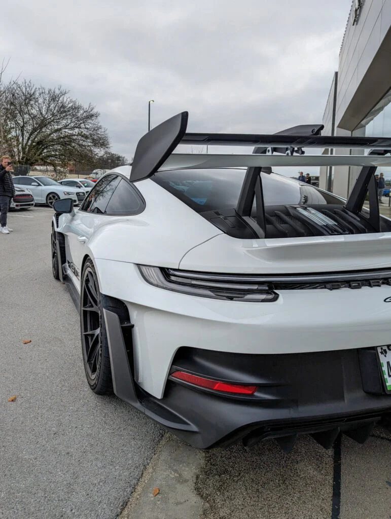 White Porsche 911 GT3 RS with a large rear wing parked in a lot with other cars.