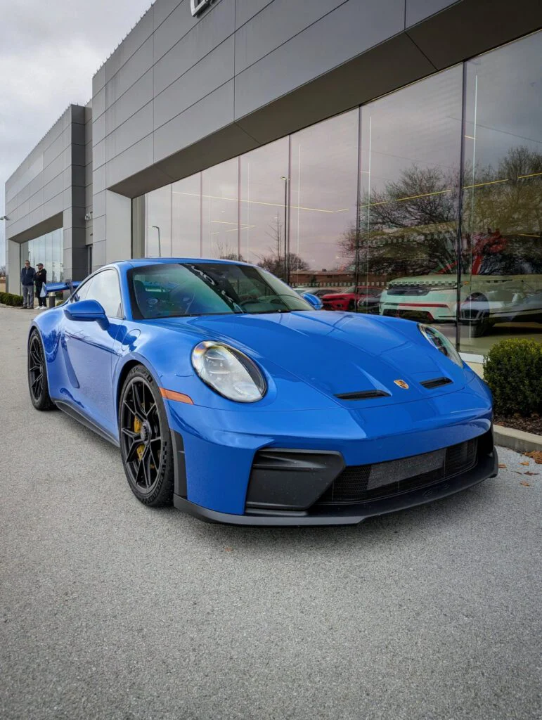 Blue Porsche 911 GT3 parked outside a modern building with large windows.