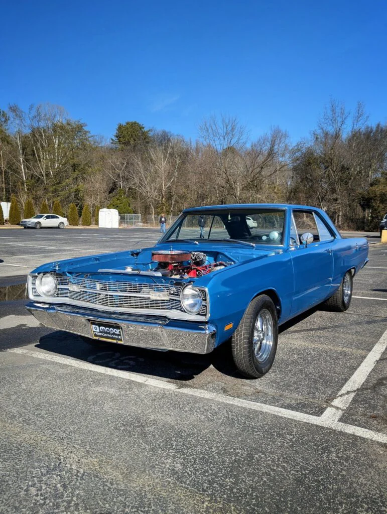 Light blue Dodge Dart displayed in a parking lot with trees in the background.
