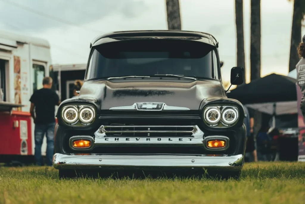 Front view of a black Chevrolet truck at a car event with food trucks in the background.