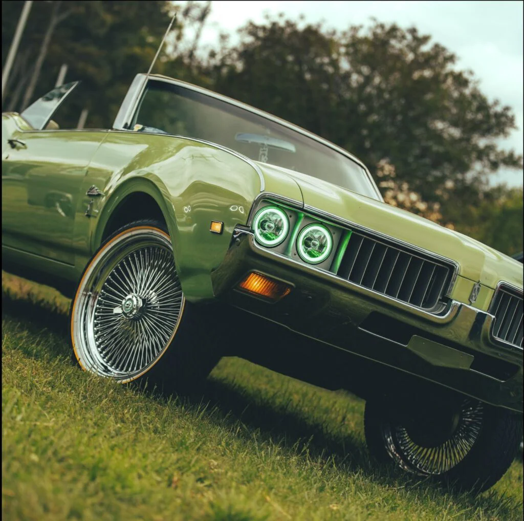 Green convertible car with chrome wheels parked on grass, showcasing custom headlights.