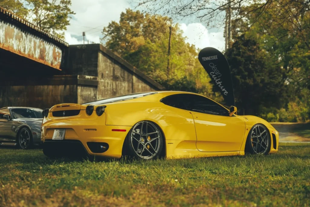 A yellow Ferrari sports car parked on grass near a rusted structure.