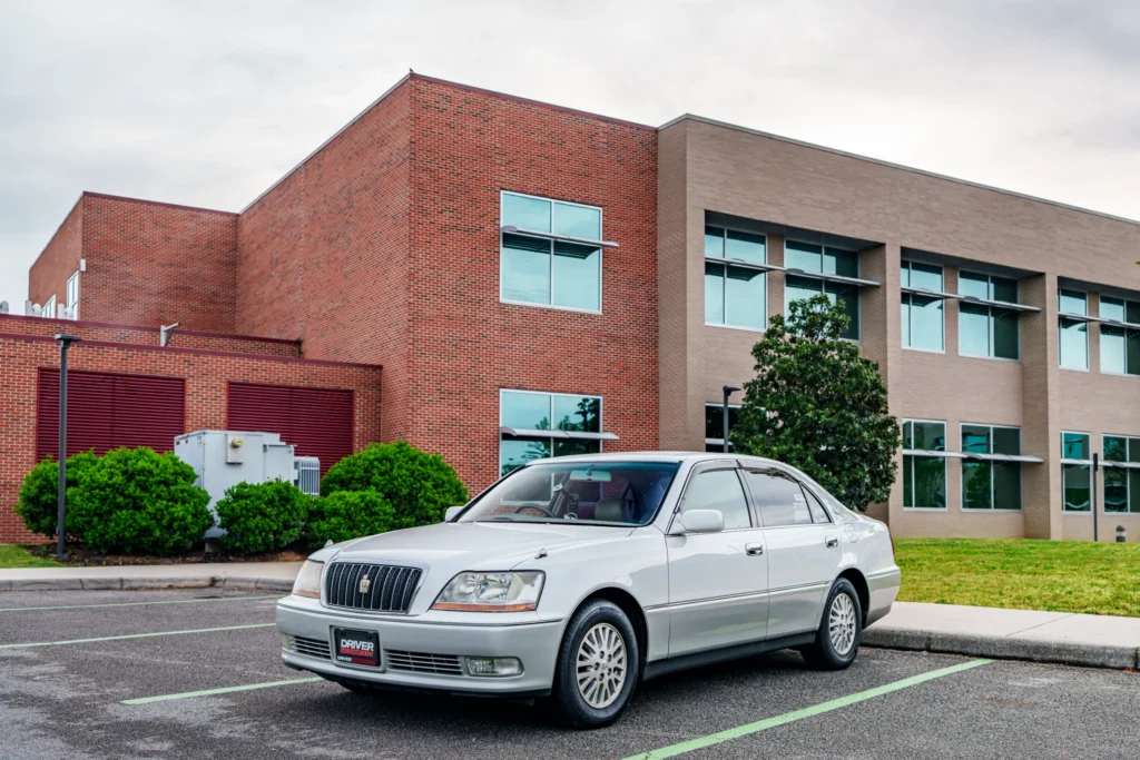 Silver Toyota Crown sedan parked in front of a commercial building with red brick and beige walls