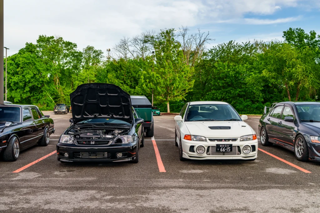 Black Honda Civic with hood open and white Mitsubishi Lancer Evo IV GSR parked side by side in a parking lot