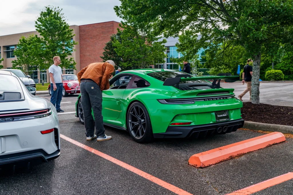 Bright green Porsche 911 GT3 with people around it in a parking lot at a car event on a cloudy day.