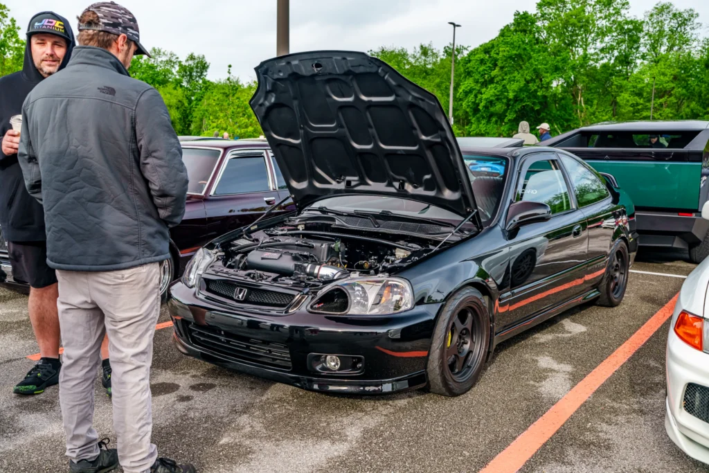 Black Honda Civic with hood open at outdoor car event with two men standing nearby