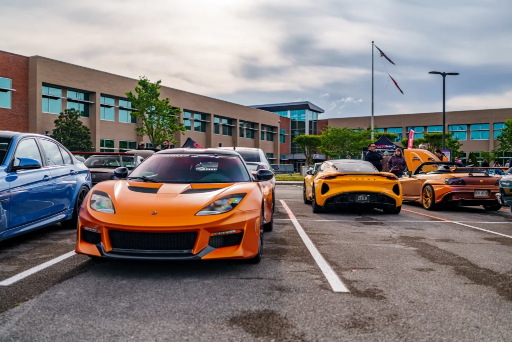 Parking lot with orange Lotus Evora and Emira and a blue car at a car event