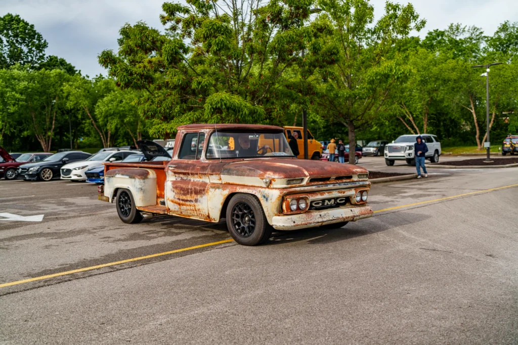 Rusty white and brown GMC pickup truck with lowered suspension in parking lot at a car meet
