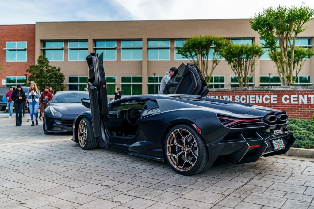 Black Lamborghini Revuelto with scissor doors open in front of a beige building and a parked gray Ferrari