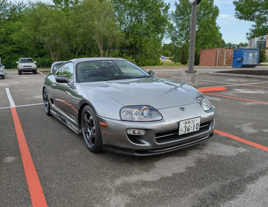 Silver Toyota Supra parked in a lot with trees and other vehicles in the background.