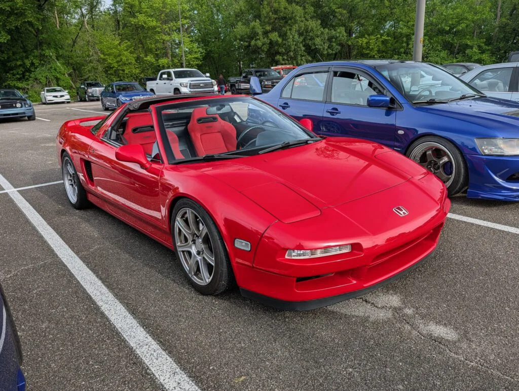 Red convertible car parked in a lot with other vehicles visible in the background.