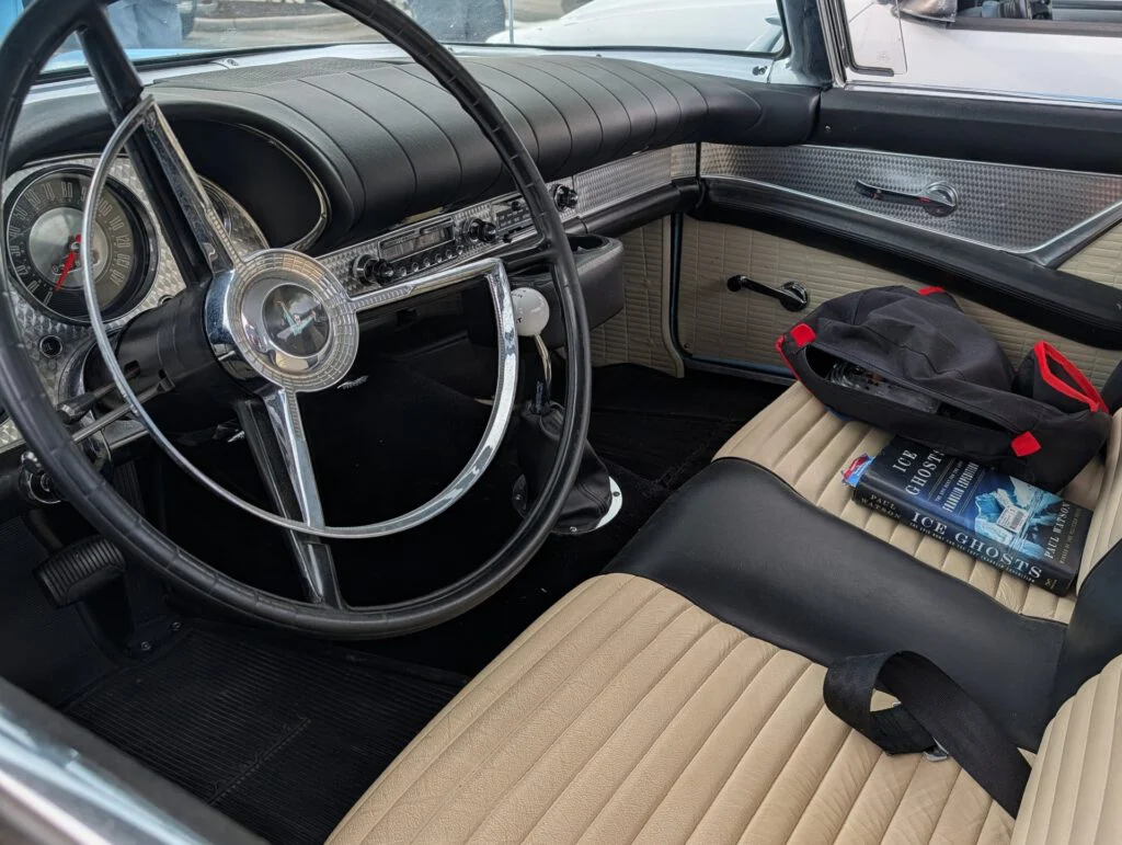 Interior of a vintage vehicle featuring a steering wheel, gauges, and tan upholstery with accessories on the seat.