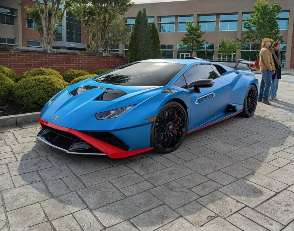 Lamborghini Huracan STO in blue with red accents parked near a building and shrubbery, with two individuals in the background