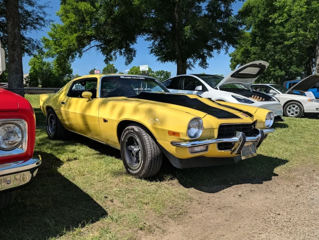 A yellow Chevrolet Camaro with a black stripe, parked at a car event next to a red vehicle.