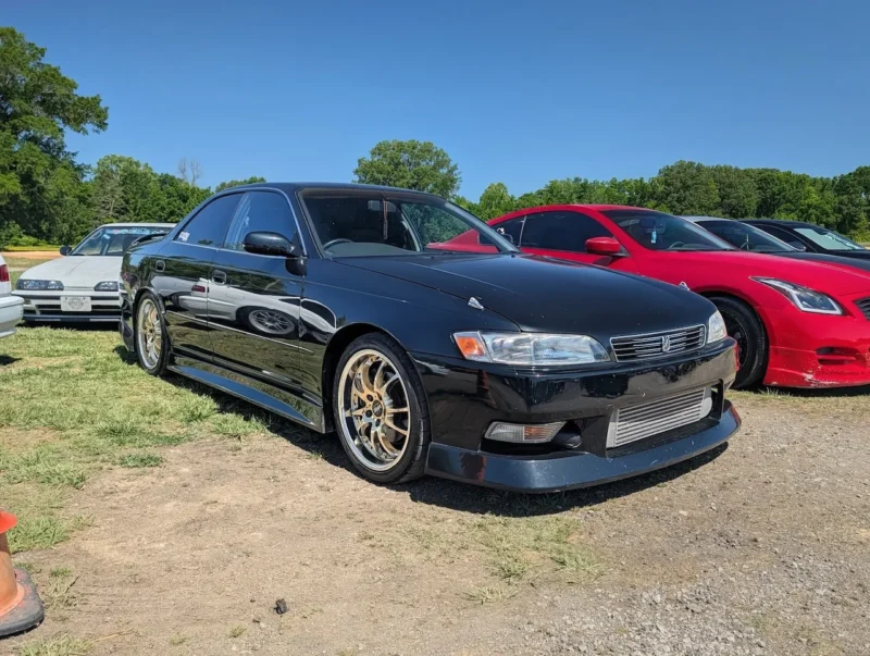 Black four-door sedan with aftermarket wheels at outdoor car event.