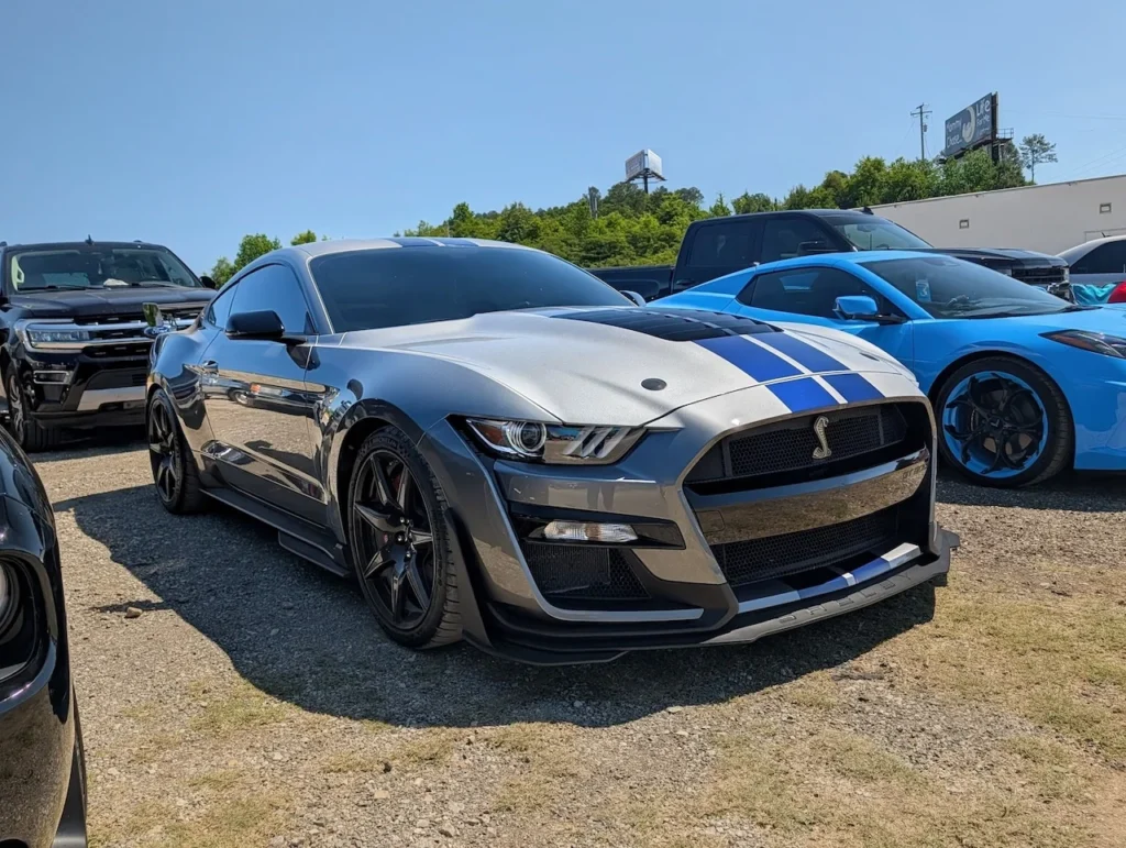 A silver Ford Mustang Shelby GT500 parked among other vehicles in a lot.