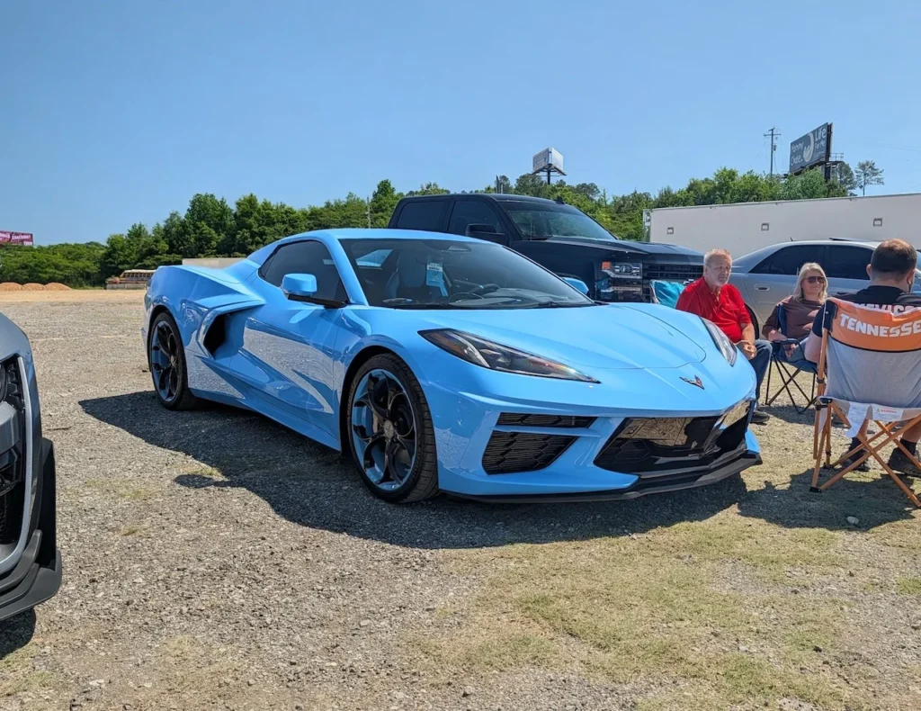 Blue Chevrolet Corvette parked outdoors with people sitting nearby