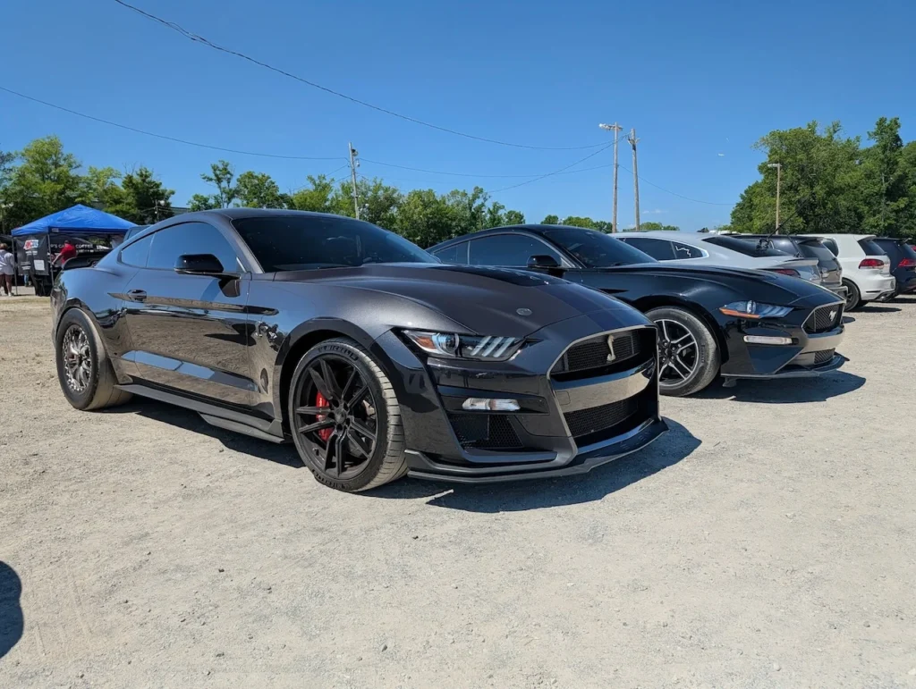 Black Ford Mustang GT500 parked on a dirt surface at a car event.