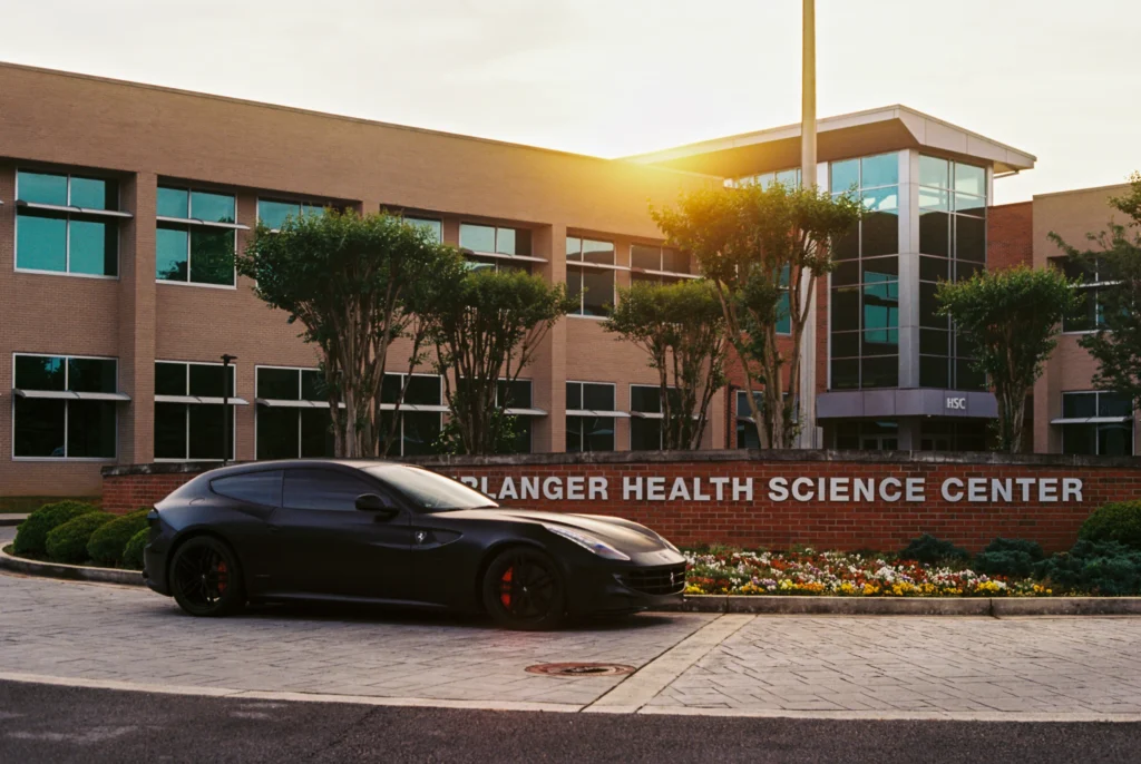 Black Ferrari FF parked outside a brick building with 'HSC' and 'Blanger Health Science Center' signage