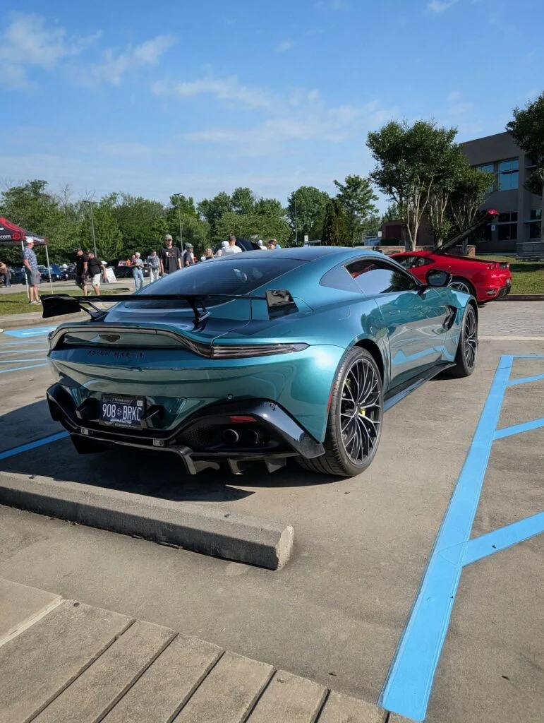 Aston Martin Vantage F1 Edition parked outdoors with people and a red car in the background