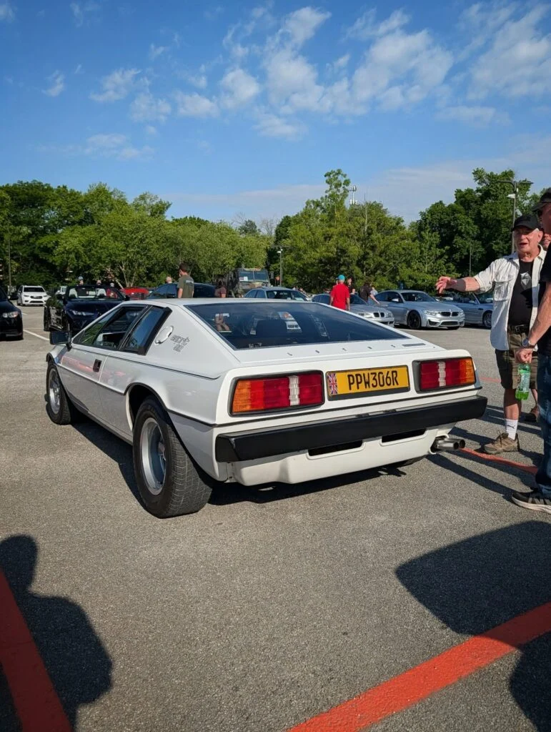 White Lotus Esprit SE parked outdoors at a car event with people walking around in background under blue sky