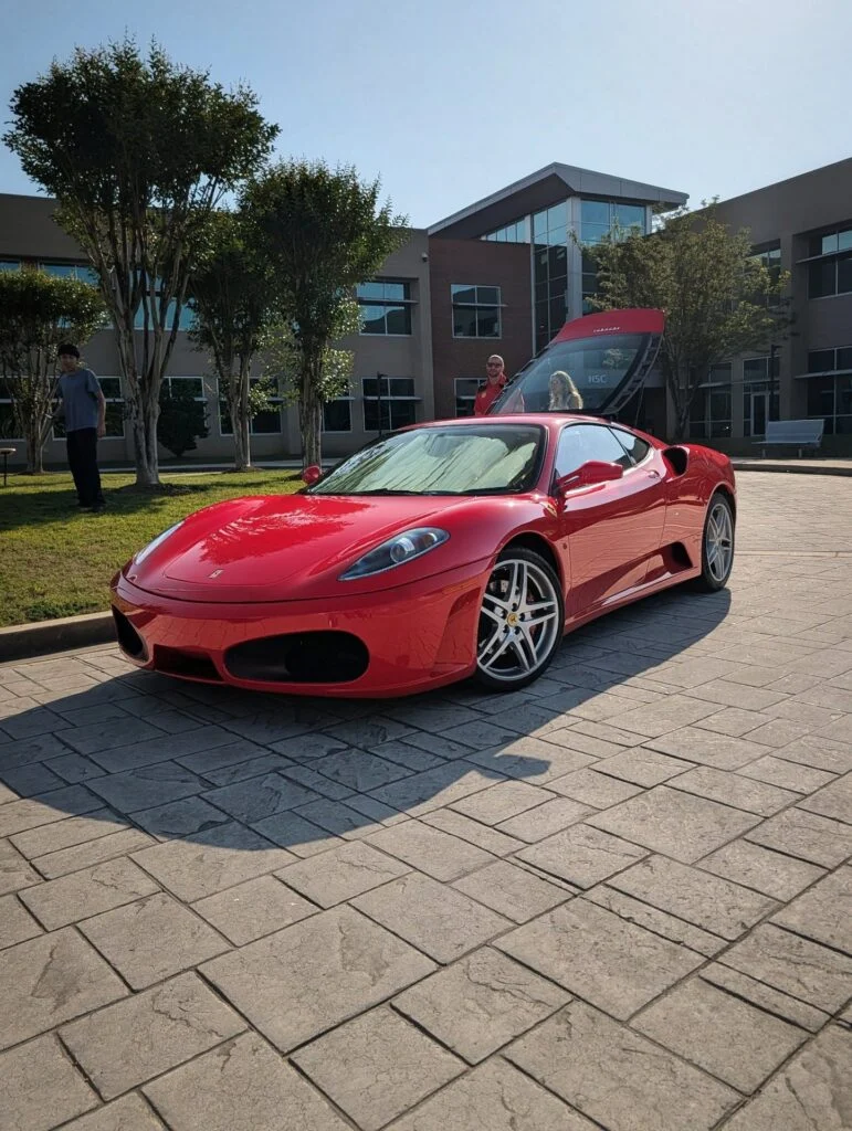 Red Ferrari F430 with rear hood open parked on stone pavement near a modern building with people around