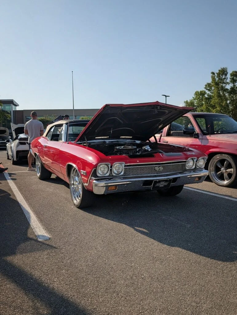 Red Chevrolet Chevelle SS 396 convertible with hood open at a parking lot car meet on a clear sunny day