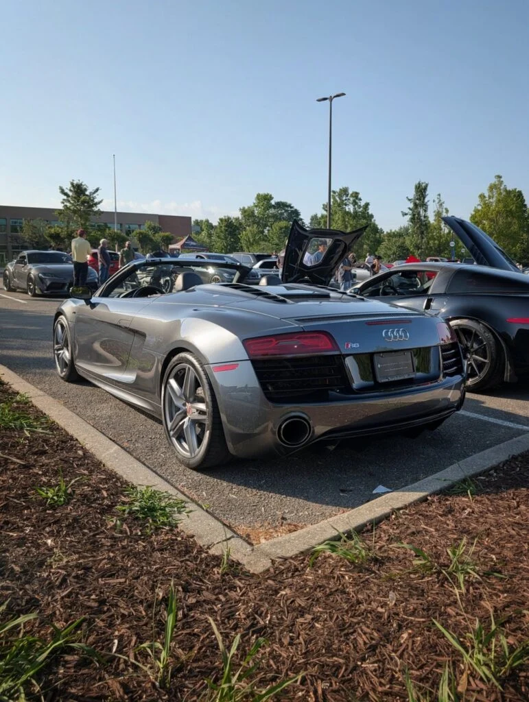 Silver Audi R8 convertible parked outdoors at a car event with other vehicles and people in the background