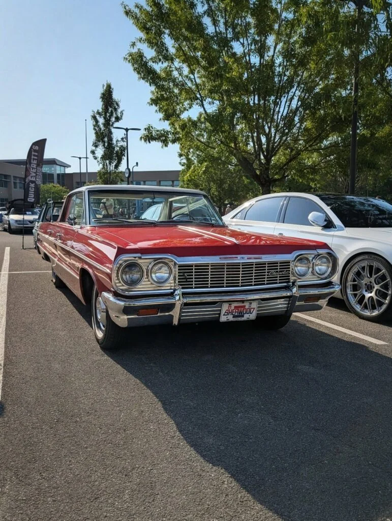 Red Chevrolet Impala parked outdoors beside a white car with trees and a building in the background