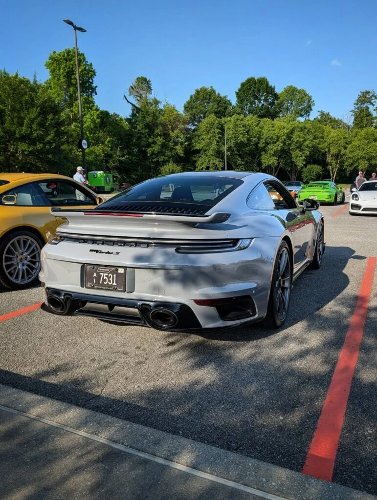 Silver Porsche 911 Turbo S parked in a lot next to a yellow Porsche coupe and other cars in the background