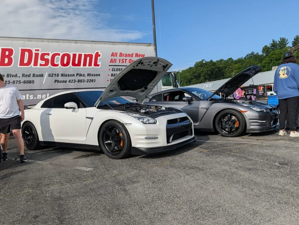 White and gray Nissan GT-R cars parked next to each other with their hoods open at an outdoor car event