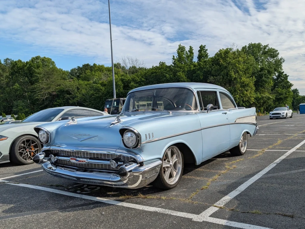 Light blue 1957 Chevrolet Bel Air parked in an outdoor lot with other cars and trees in the background