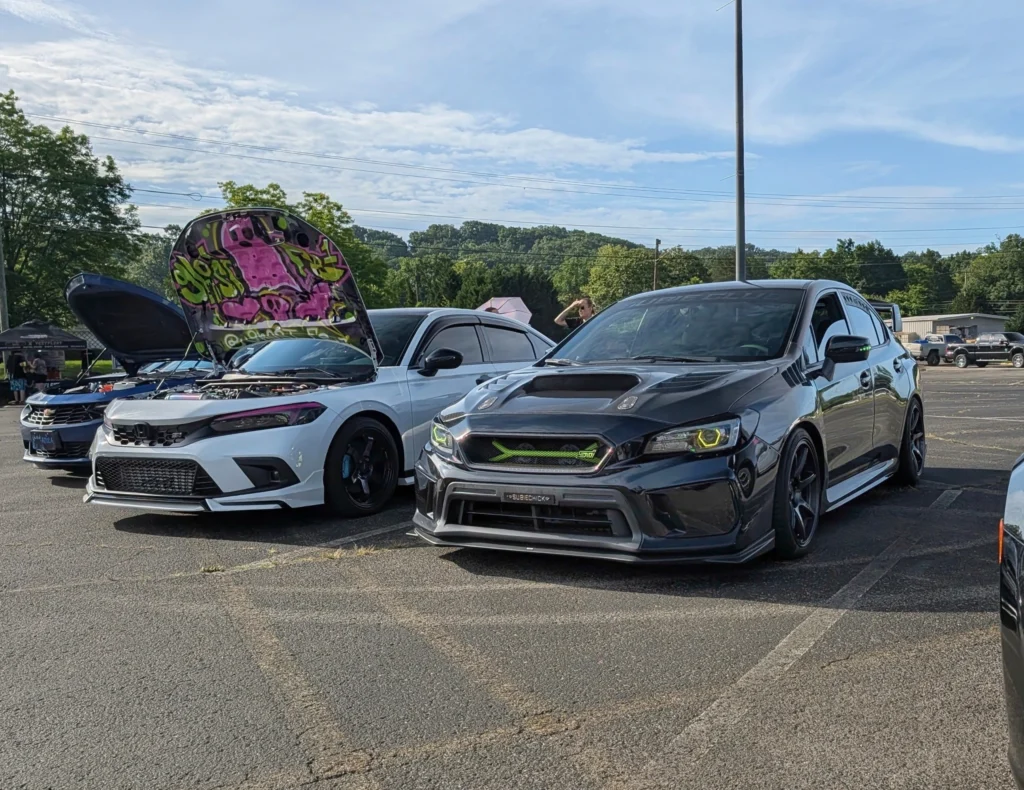 White Honda Civic Si with custom painted hood and black wheels parked next to a black Subaru WRX STI at car event