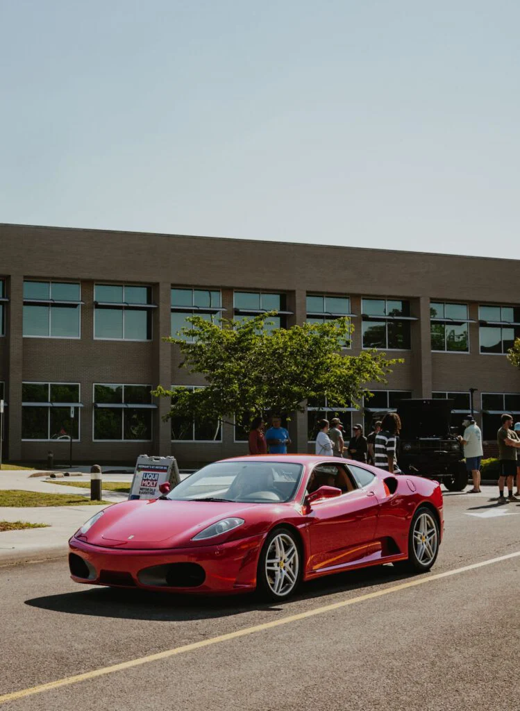 Red Ferrari F430 parked on street in front of a brick building with people gathered nearby