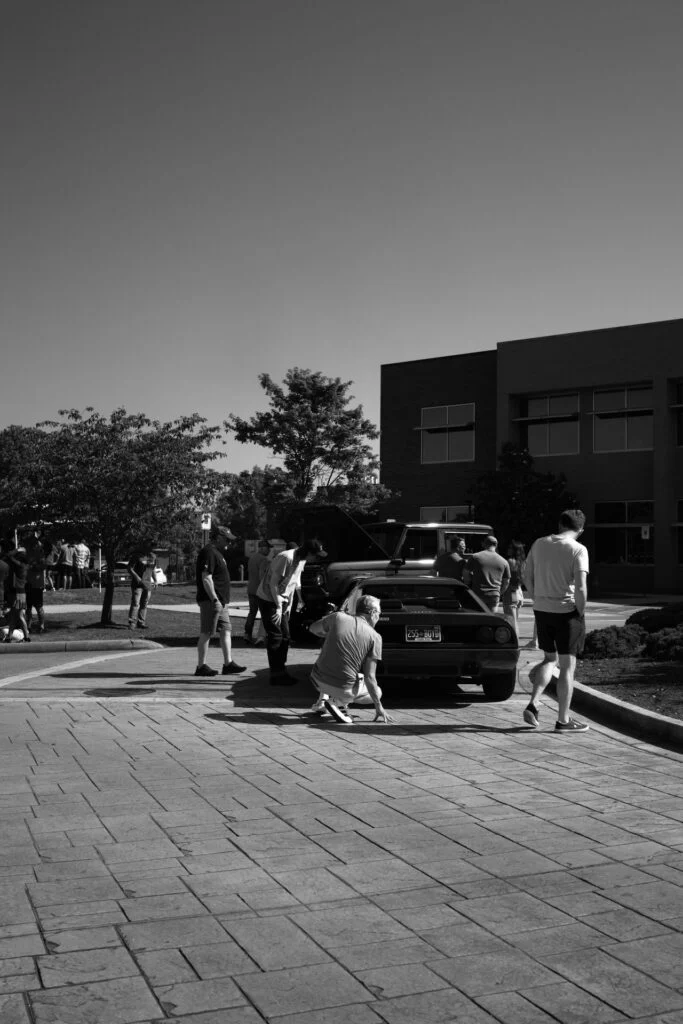 Ferrari 512 BB surrounded by people at an outdoor car event near a building.