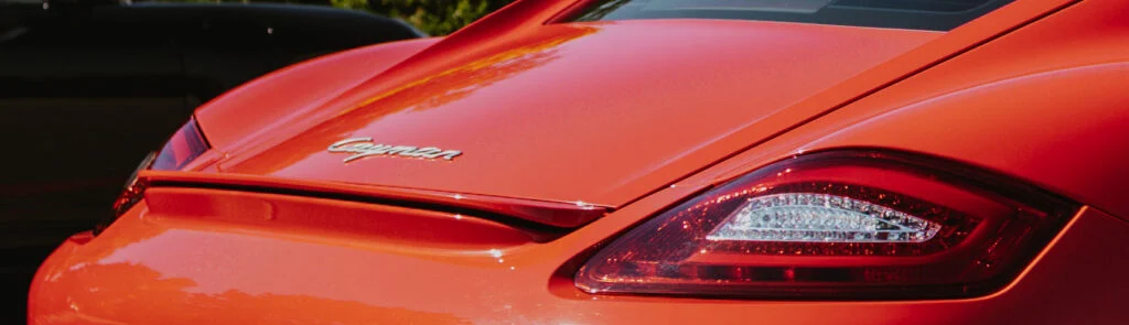 Rear section of an orange Porsche Cayman showing the model script and left taillight in daylight