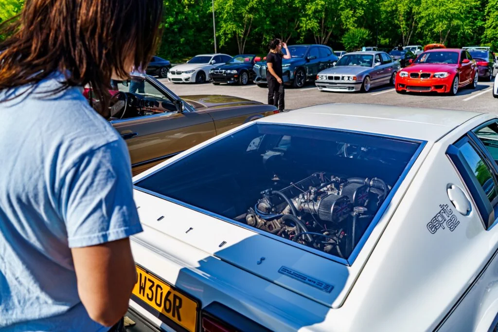 White Lotus Esprit S2 with exposed engine in rear and surrounding parked cars at outdoor car event