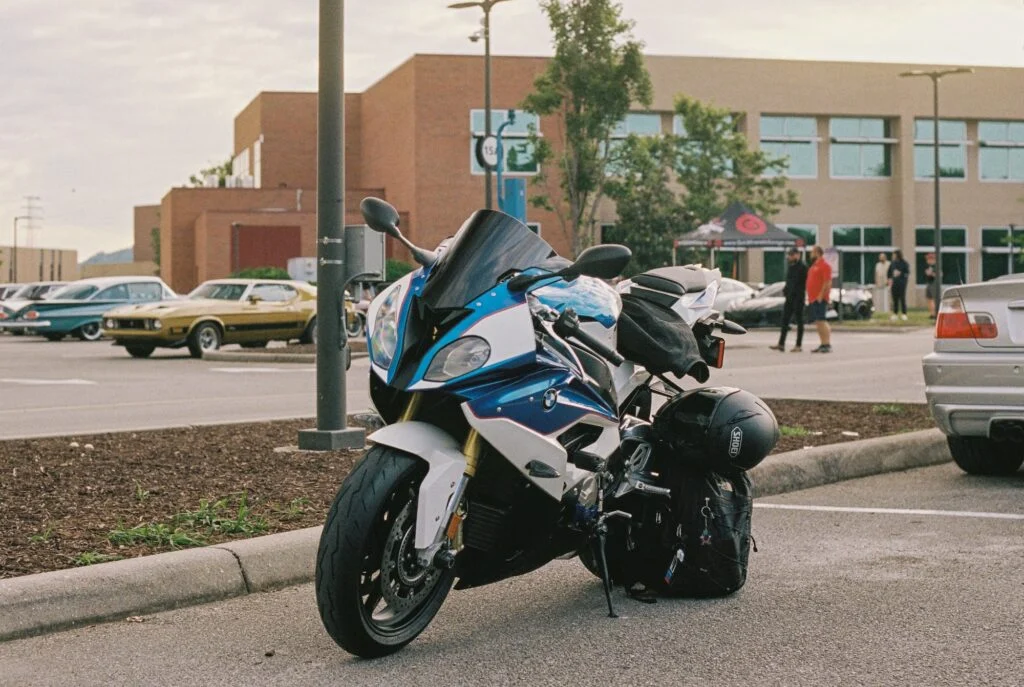 White and blue BMW S1000RR parked in a lot with classic cars and people in the background at an automotive event