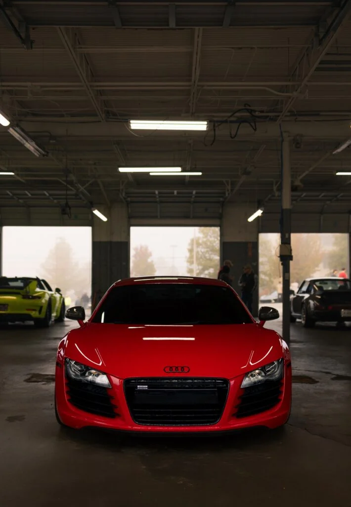 Red Audi R8 parked inside garage with a yellow Porsche 911 in the background through open garage doors