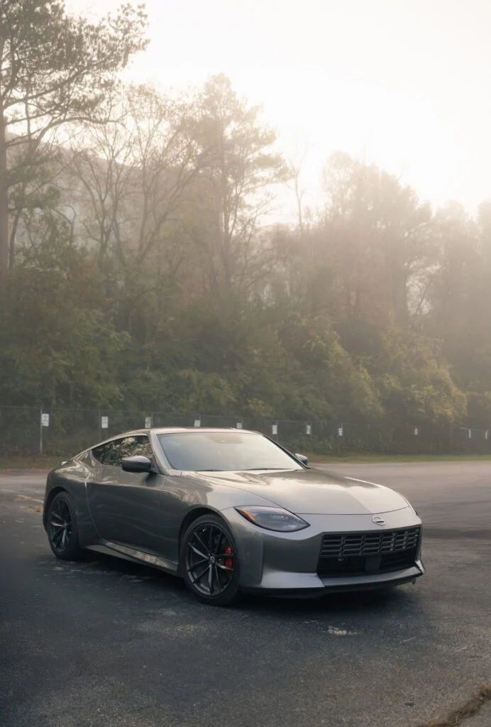 Gray Nissan Z sports car parked on asphalt with trees and fog in the background