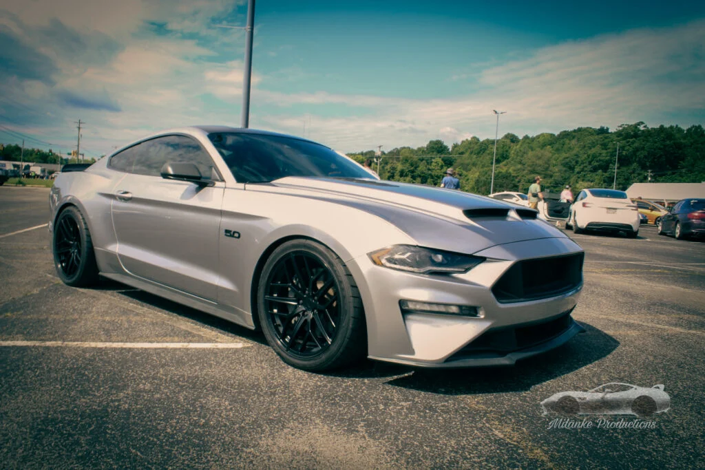 Silver Ford Mustang GT parked in an outdoor lot with trees and other vehicles in the background