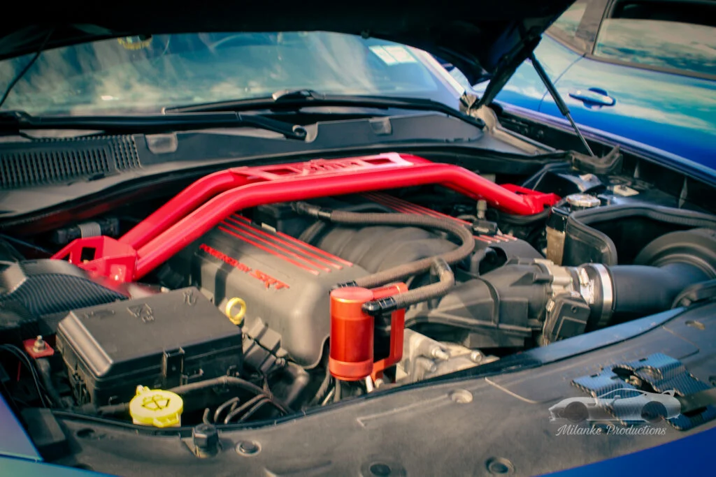 Engine bay of a vehicle with a red SRT strut bar and various engine components visible