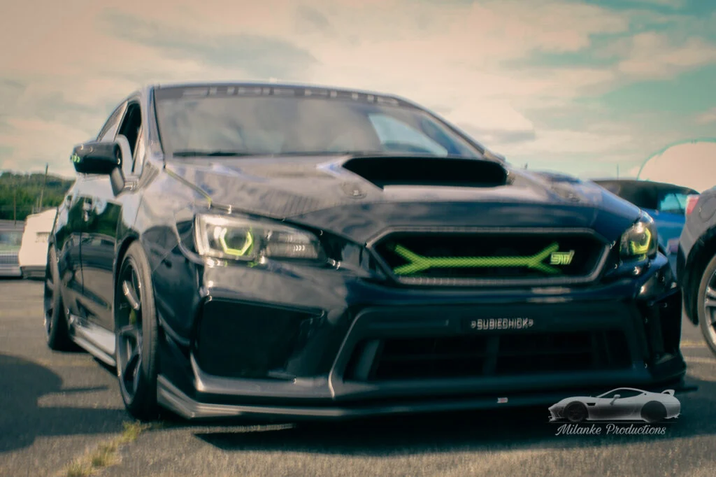 Black Subaru WRX STI parked outdoors with green-accented headlights and grille on a cloudy day