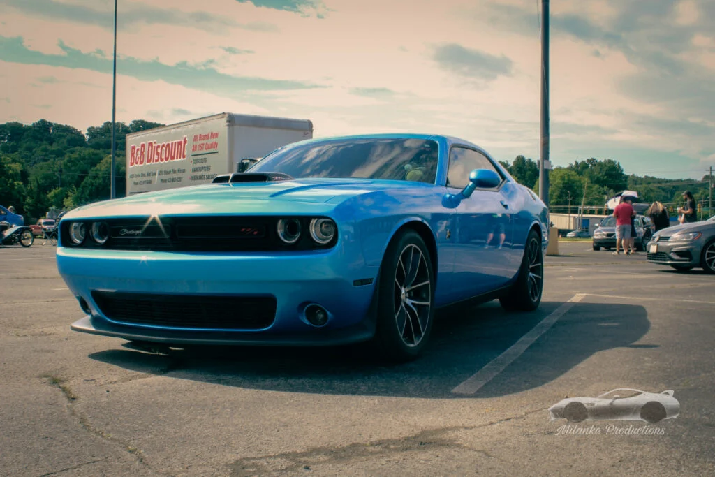 Blue Dodge Challenger R/T parked at an outdoor car event with other cars and people in the background