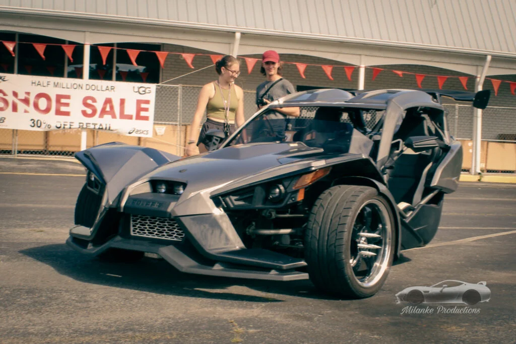 Gray Polaris Slingshot three-wheeled vehicle parked outdoors with two people standing nearby